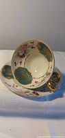 Teacup resting in saucer showing interior floral and turquoise gilt design