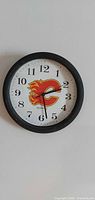 Front view of round wall clock showing Calgary Flames logo, black frame, white dial