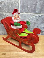 Santa doll seated in red wooden sleigh, front angle