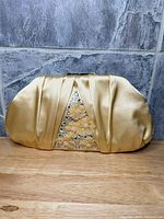 Front view of gold satin Badgley Mischka frame clutch showing pleats and embellished triangular panel