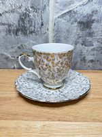 Cup on saucer, front view showing gilt floral design and shape