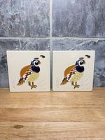 Both ceramic tiles side by side on wood surface, quail relief visible