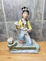 Front view of glazed porcelain woman figurine on rock-form base with basket