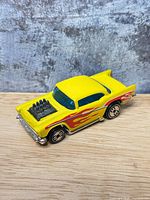 Left side view of yellow Hot Wheels 1957 Chevy Bel Air with exposed engine and flame livery