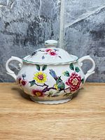 Front view of covered sugar bowl showing floral and bird pattern, twin handles and lid
