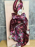 Full view of porcelain-faced jester doll mounted on backing