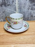Cup on saucer front view showing floral design and gold handle