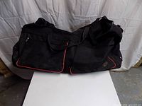 Front and top view of black rolling duffel showing handles, pockets, red piping