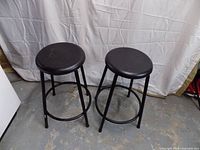 Front view of both black metal bar stools showing seats and frames