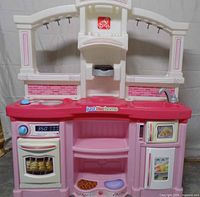 Front view of Step2 play kitchen showing sink, stovetop, oven, microwave, shelves, pink and white color scheme