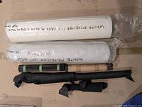 five rolled materials on surface: two white polyester fabric rolls and three black leather rolls