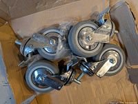 Top view of five unused swivel casters in box with mounting hardware bag visible