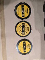 Top-down view of three new DeWalt 12" circular saw blades showing labels and condition