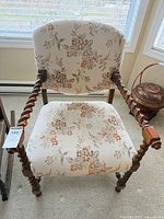 Front view of upholstered armchair showing floral fabric, wood frame and barley-twist legs and arms