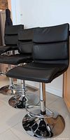 Three black faux leather Eztia bar stools in a row showing fronts and chrome bases