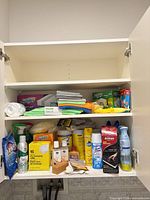 Cabinet showing two shelves of assorted cleaning supplies and cloths