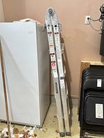 Full view of folded aluminum ladder leaning against fridge