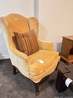 Front angled view of gold velvet wingback chair with striped pillow