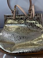 Front view of gold metallic MK tote showing exterior pattern and straps