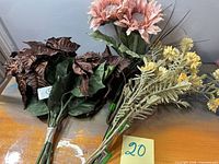 Three grouped bundles of artificial stems: brown leaves, pink bloom, yellow flowers with green grass, tags visible