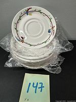 Stack of eight saucers wrapped in plastic with visible floral border pattern