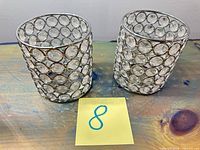 Two cylindrical silver crystal light trim covers on table