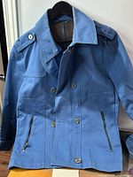 Full view of front of blue trench coat showing buttons, zippers and collar