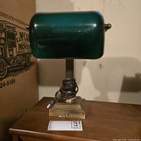 Front view of banker’s lamp on table showing green glass shade and brass-tone base