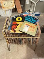 Stack of vinyl records on metal rack with several records displayed on top showing artists and labels