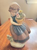 Front view of porcelain figurine showing girl, flower pot, and foliage base