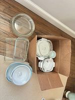 Group view showing clear Pyrex round pie plate, two Pyrex loaf pans, boxed CorningWare casseroles with lids