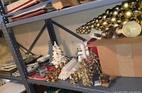 Shelf view showing brass candle holders, plastic candle sleeves, ceramic trees, gold beads, pinecones