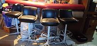Four black vinyl swivel bar stools lined up in front of bar