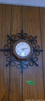 Wall clock with metal scroll surround on wood paneling