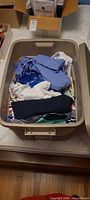 Beige plastic tote filled with folded women’s clothing in assorted colors and patterns