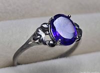 Side view of ring showing silver-tone band and prong-set oval purple stone
