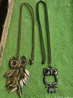 both owl necklaces side by side on green background
