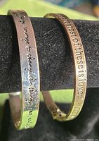 Both bracelets side by side on display bar showing exterior engravings