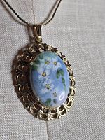 close-up of floral painted cabochon pendant in gold-tone bezel on chain