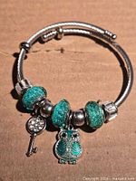 Bracelet front view showing teal glitter beads, owl and key charms