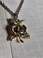 Close-up of gold-tone rose pendant showing petals, leaves and stem detail