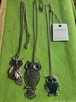 Three owl necklaces laid out showing pendants and chains; tagged item visible