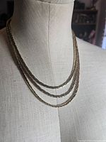 Necklace displayed on bust showing triple strands and gold-tone finish