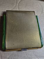 Front view of closed gold-tone cigarette case with green side strips