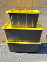 Three stacked black plastic totes with yellow lids