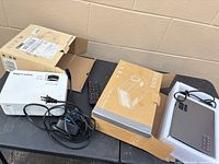 Both projectors on table with boxes, cords and remote visible