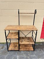 Front view of baker’s rack showing wood shelves, wire basket and metal frame