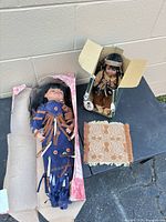 Both dolls in boxes and woven rug on table