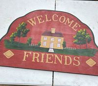 Front view of arched wooden welcome sign with painted house, trees and text