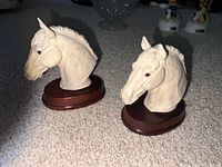 Two cream horse head busts on wood bases side by side